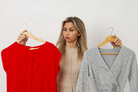 A pretty woman can not choose a dress on a white background Which dress to choose silver or redの写真素材