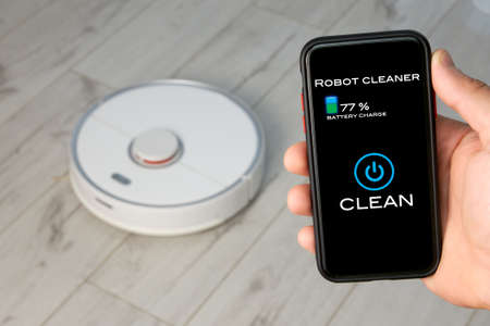 A person using the remote control of a Robotic Vacuum Cleaner on their smartphone. Smart Life Technology Conceptの写真素材