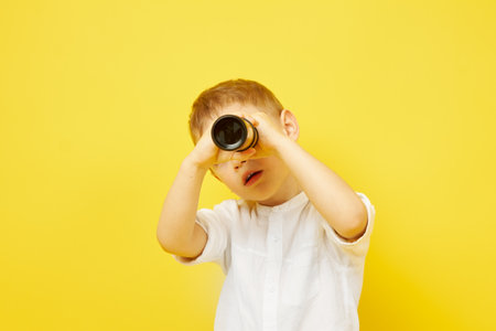 The boy looks through a telescope on a yellow background. The concept of travel, pirates and adventures, active lifestyle, striving for the goalの写真素材