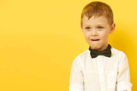 The boy looks thoughtfully into the distance. A child in a bow tie and a white shirt on a yellow background.の写真素材