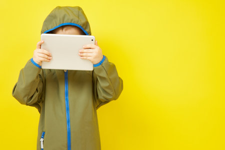 A boy wears headphones while using a tablet computer on a yellow backgroundの写真素材