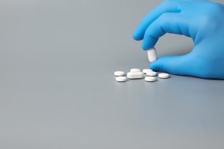 A blue-gloved hand holds a white pill against a gray background. Demonstration of pill selection