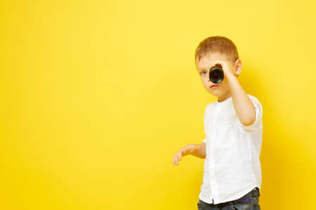 The boy looks through a telescope on a yellow background. The concept of travel, pirates and adventures, active lifestyle, striving for the goalの写真素材