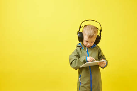 E-learning. A small boy with headphones is studying a tablet computer on a yellow background