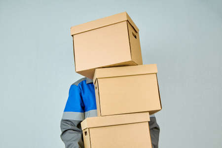 A loader or courier transports cardboard boxes along the blue wall in work clothes. Moving day....
