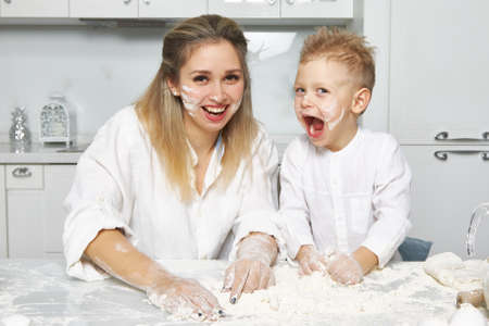 Happy mom and boy in white kitchen smeared face with flourの写真素材