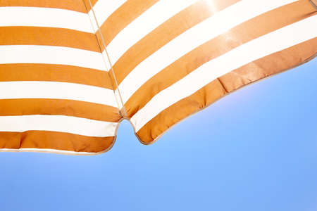 Striped sun umbrella against the blue sky. Concept of summer hotel holidays, beach holidays, tanning
