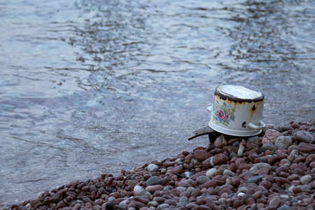 Rusty old pot on the pebble beach near the waterの写真素材