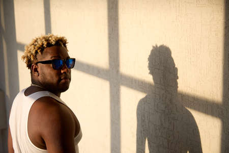 Cool black man in dark glasses, a white T-shirt and his shadow on the wallの写真素材
