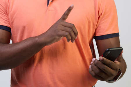 Close-up of an African-American man on a white background holding a smartphone, typing a message, communicating with friends or relatives, playing an online game, making purchases.の写真素材