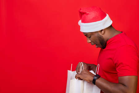African-American man in a Santa hat and a red T-shirt opened his mouth in surprise, looks into white...