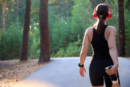 Athlete is a runner, stretching her legs and feet and preparing to run on an asphalt road in the forest. Active, running training and the concept of a healthy lifestyle in sports.の写真素材
