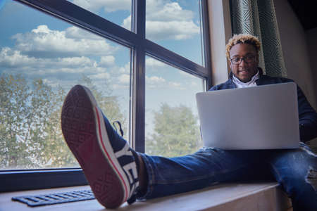 An African-American man in casual clothes and glasses is browsing the Internet on a modern laptop,...
