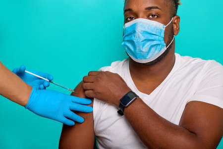 Hands in blue gloves inject the vaccine using a syringe with the vaccine into the arm muscle