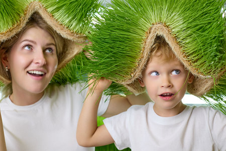 Blue-eyed boy and a young woman are enjoying the sprouts of fresh greenery. Child and his mother look up at the green patch of wheat plantation on his head.の写真素材