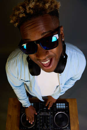 An African-American DJ with an Afro hairstyle plays music with sunglasses and headphones. On its own wave. Enjoys his occupation. Professional black man DJ.の写真素材