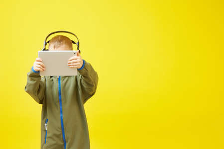 A boy wears headphones while using a tablet computer on a yellow backgroundの写真素材