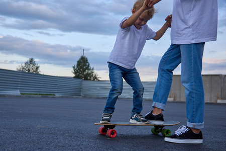 A teenager in white t-short in sneakers teaches a boy in the street how to ride the skateboard.の写真素材