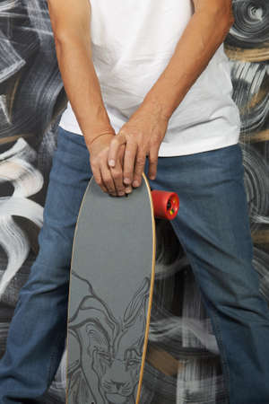 Legs of a fashionable man in jeans and sneakers with a skateboard in his hands close-up. A man poses against a painted wall. Vertical photographyの写真素材