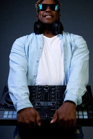 Handsome black man in a blue shirt holds a DJ mixer for recording. Men in sunglasses and headphones.の写真素材