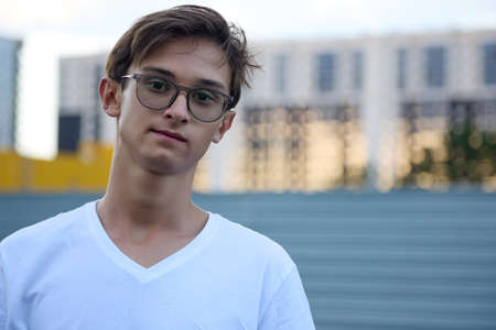 Handsome boy with glasses smiles at the camera against the background of tall multi-storey...