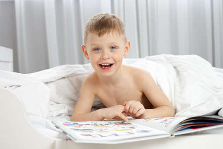 A sleepy boy lying under a blanket looks at pictures in a white baby cotの写真素材