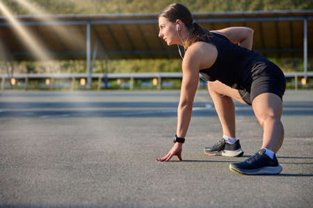 Portrait of a fit and athletic young woman in headphones and black sportswear doing stretching at...