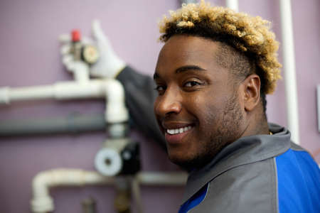 Close-up of a happy African man who loves his job, checks the pressure on the sensor in the boiler...