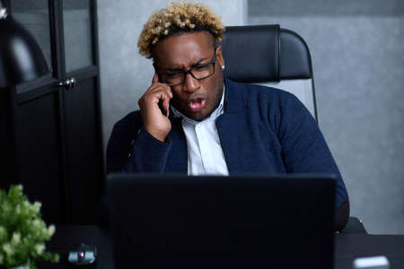 Angry businessman with glasses shouts into the phone during negotiations and looks at the laptop....