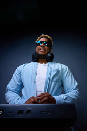 African-American DJ wearing headphones and sunglasses works in a studio in a dark room. Top-down view.の写真素材