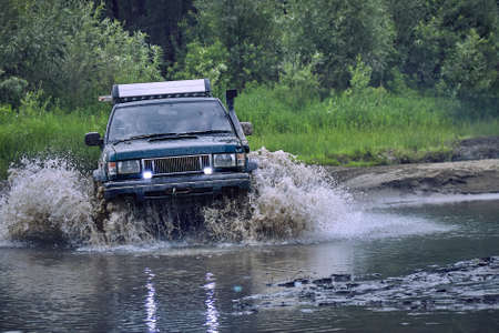 Off-road 4x4 car overcomes a small river at high speed, splashes from under the wheels when moving through. The concept of extreme and adventureの写真素材