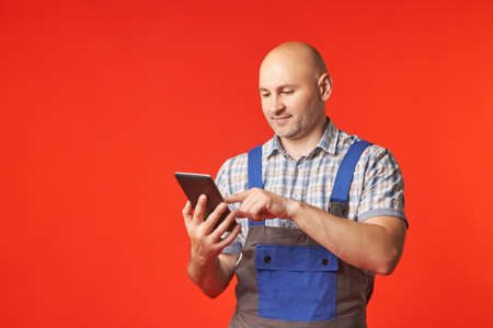 Bald man in a work suit holds a phone with one hand and works in it with the other, a photo on a red background. The employee accepts orders using the phoneの写真素材