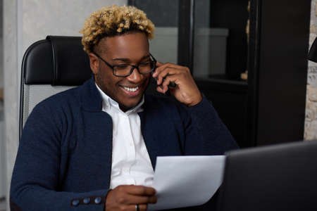 Smiling African-American businessman with glasses holds documents or reports in his hands, examines...
