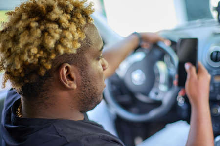 Close-up of a young African man or a driver with a smartphone in his hand at the wheel of a car....
