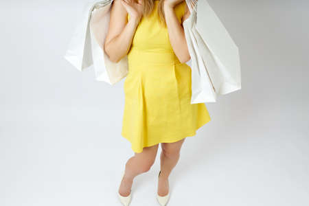 Beautiful young woman in beige shoes and with shopping bags in her hands on a white background. A...