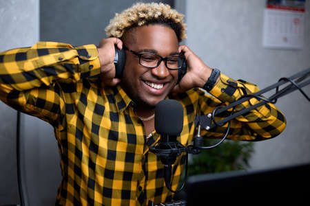 African musician enjoys listening to his new track with headphones. A black man with glasses smiles while listening to a melody recorded in a home studioの写真素材