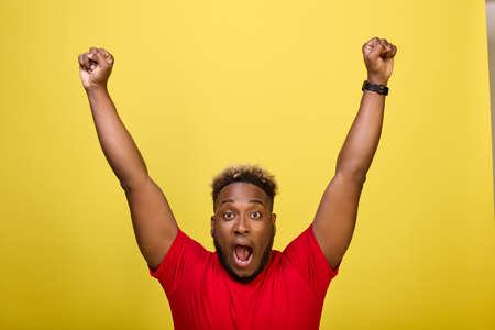 Black fan rejoices at victory of his favorite team at stadium. Young black athlete in red T-shirt...