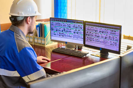 Worker in overalls uses a linear telemechanics system to control the technological processes of the enterprise. Automated workplace of a dispatcher or operator of a modern enterpriseの写真素材