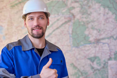 A smiling Caucasian worker in overalls and a helmet on the background of the map shows a thumbs up gestureの写真素材