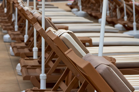 Wooden brown chairs for sunbathing stand in a row by the pool. Tourists who come to rest, after swimming in the pool, can sunbathe on sun loungers with soft mattresses and headrestsの写真素材