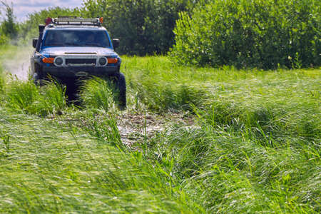 Sports car with four-wheel drive rushes through the green grass. Off-road 4x4 SUV in blue color at...