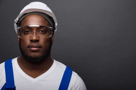 Close-up portrait of a handsome serious locksmith in a white helmet on a gray wall. In a white...