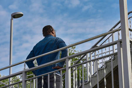 Slowly with short stops, a guy with an African hairstyle climbs a steep staircase to the mountain. Walking through the city, a young man steps up the bridgeの写真素材