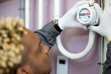 Rear view of a specialist in overalls and white gloves who checks the meter in the boiler room. The...