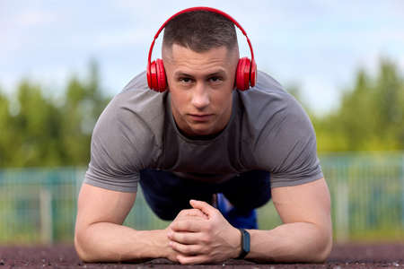 Young muscular athlete stands in the plank position, performs the exercise for a while. Strong cute...