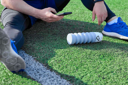 Athlete sits on lawn in stadium and takes picture on phone camera of water bottle lying next to him...
