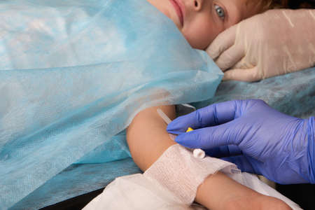 Patient child lies on the operating table with a medication catheter in his hand. Close-up of a...