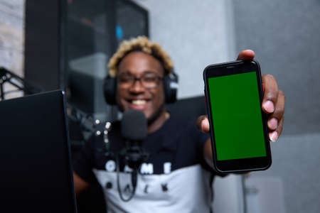 Happy African man holds a smartphone and demonstrates the good ones on his screen while sitting at...