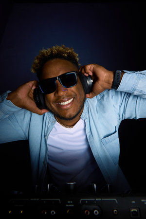 An African American man in glasses smiles and holds headphones with his hands, which have a smart...
