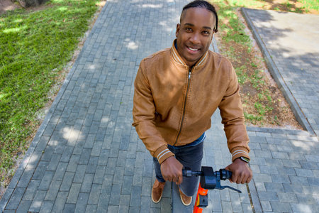 View from above of a stylish African-American man walking on a scooter through the city streets....
